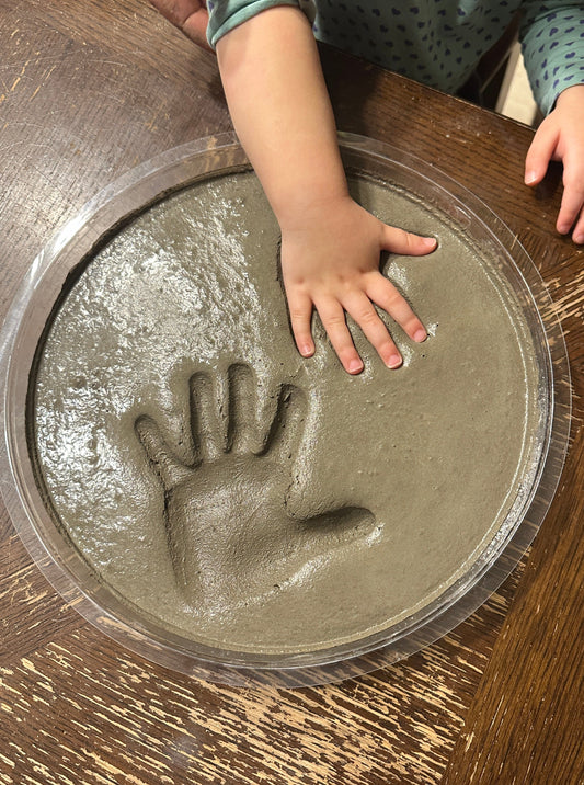 Make your own cement hand or foot print. DIY Kit Stepping Stone. This shows a child's hand being pressed into the wet concrete. Press the hand in deep to give the stone a great look once dry.  Kid's may need help from parents when pushing hand down. 