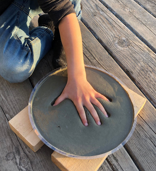 Make your own cement hand or foot print. DIY Kit Stepping Stone. This shows a child's hand being pressed into the wet concrete. Press the hand in deep to give the stone a great look once dry.  Kid's may need help from parents when pushing hand down. 